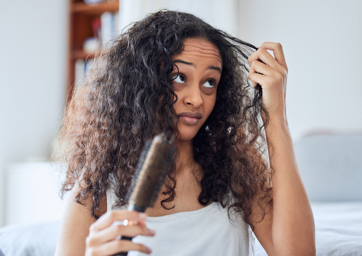 Woman in a white tank top in her bedroom trying to brush her thick, curly hair