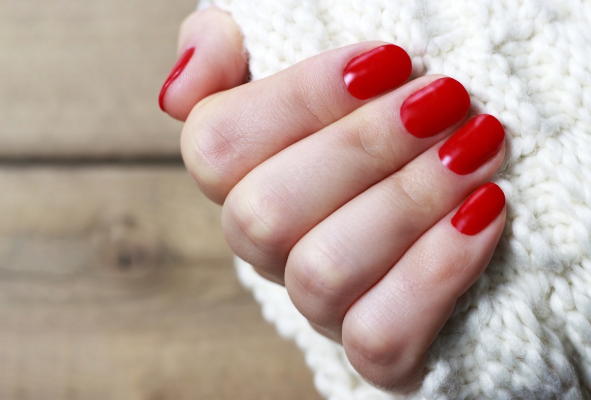 Female hand with red manicure on a white knitted background with copy space, top view