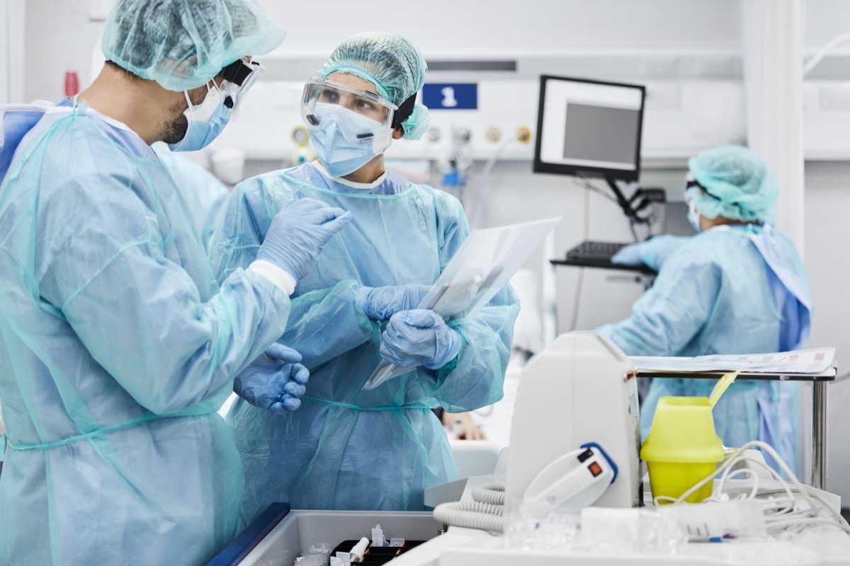 Male and female doctors discussing while standing in ICU. Healthcare workers are protective workwear. They are at hospital.