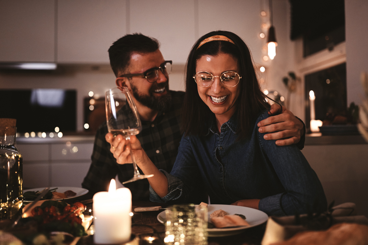 Laughing young woman drinking wine while sitting with friends around a table during a candlelit dinner party