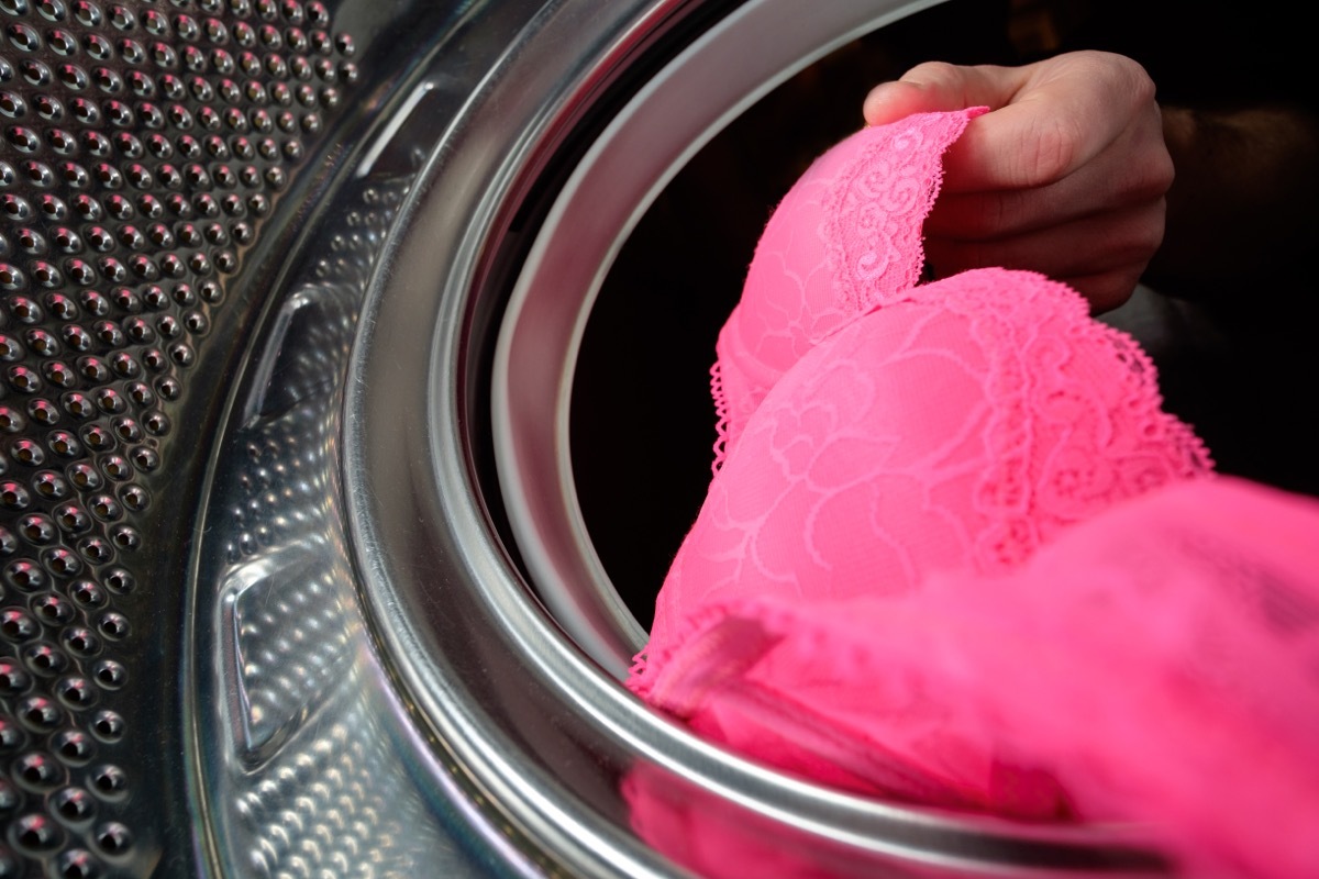 A man puts a pink bra in the washing machine, dirty clothes.