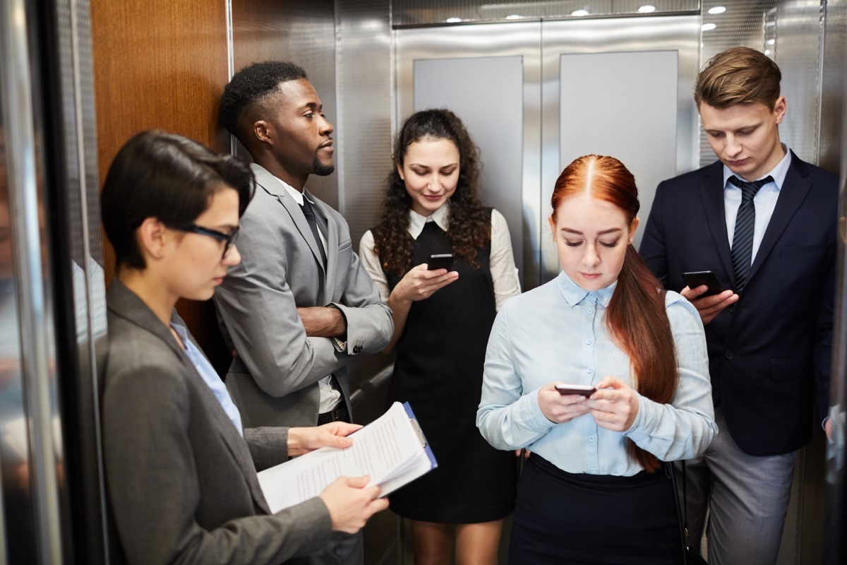 Multiethnic men and women using smartphones while standing in elevator of office