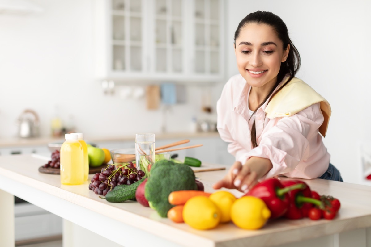 Healthy Food To Boost Your Immune System. Beautiful smiling young woman cooking fresh organic salad at home in modern kitchen, reaching for vegetables