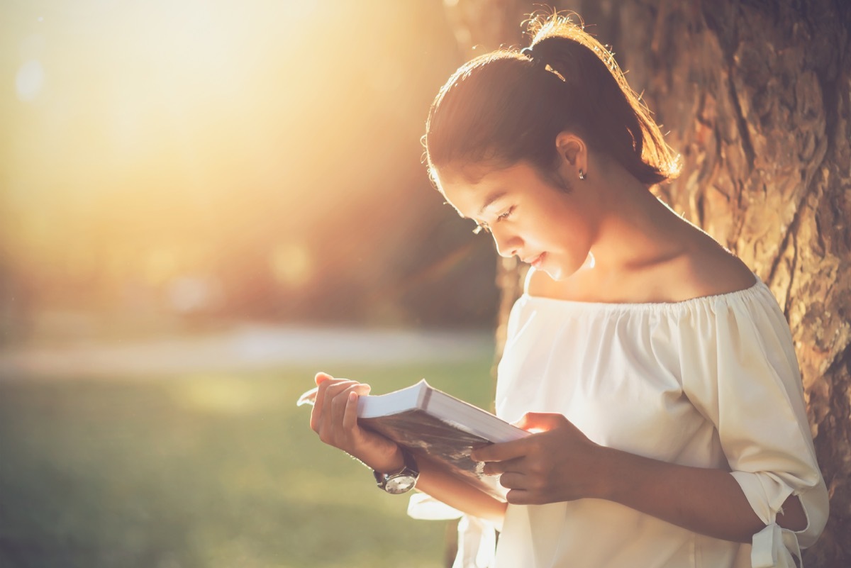 woman reading a book and leaning against a tree