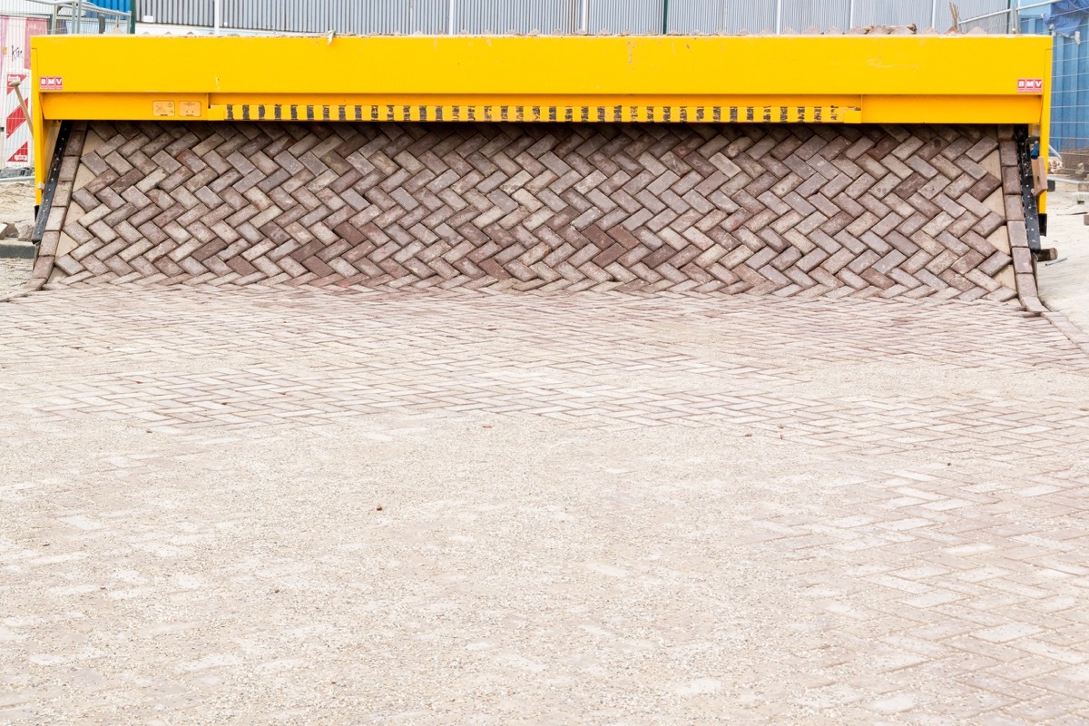 a machine printing out a brick road and laying it down