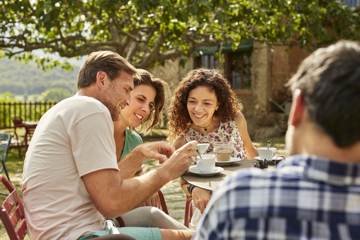 man shows his friends his cell phone while having coffee outside