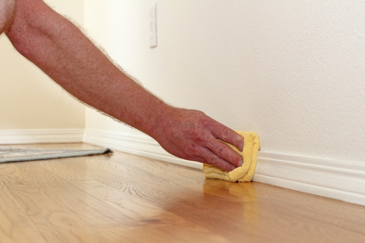 Man cleaning baseboard with cloth