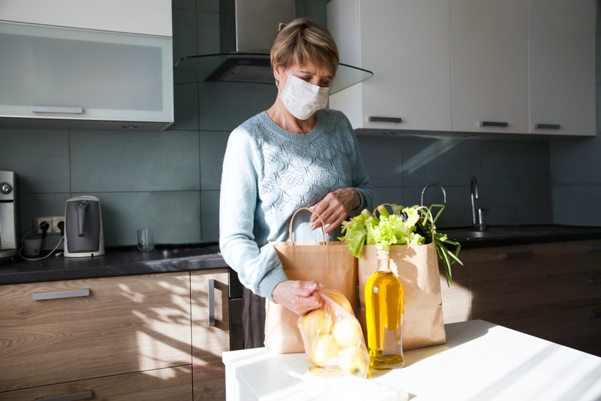 senior woman wearing a mask puts away groceries