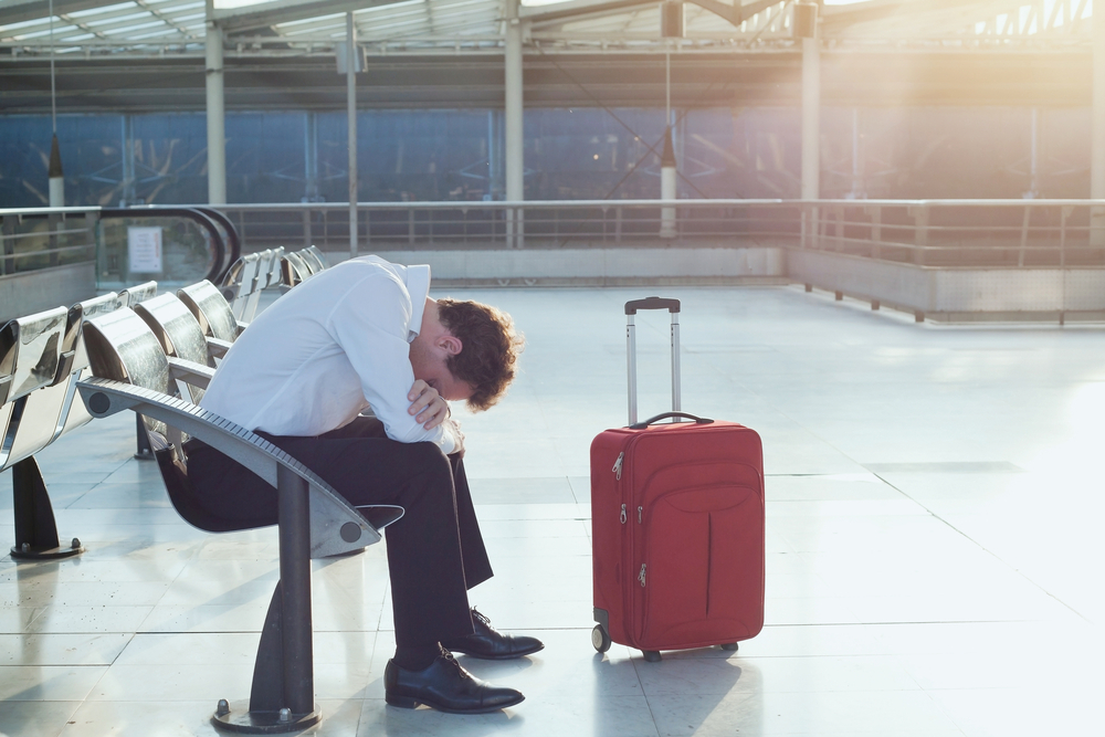 A man sitting near his suitcase in an airport after his flight was delayed or canceled