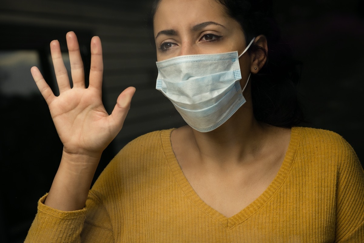 sad woman wearing a face mask looking through the window