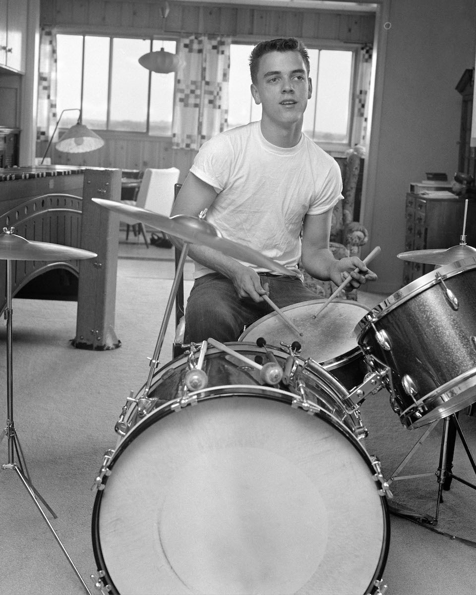 1960s TEEN BOY WITH BUZZ CUT IN T-SHIRT SITTING IN FRONT OF SMALL DRUM KIT HOLDING STICKS OVER SNARE