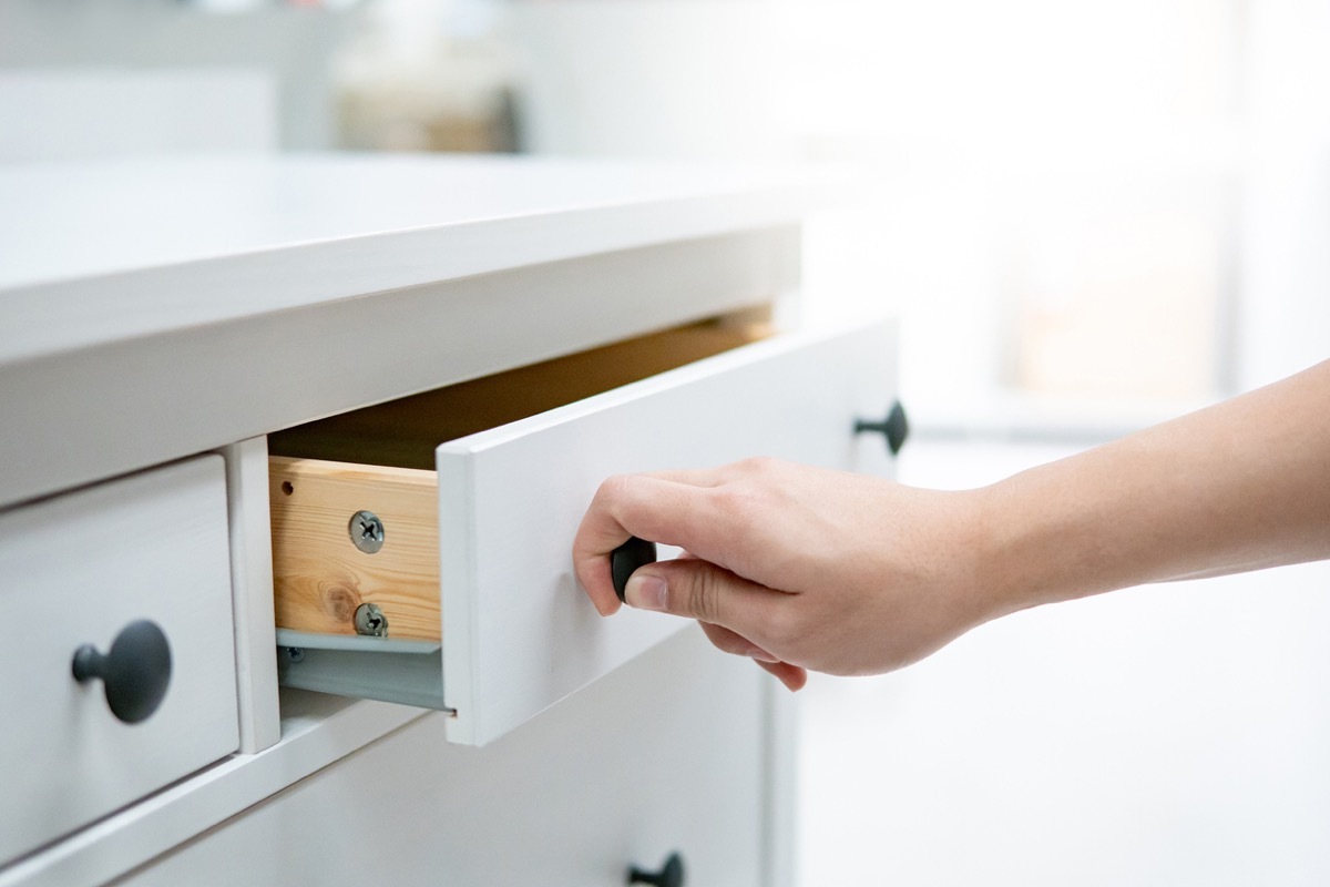 white man opening white kitchen drawer with black knob