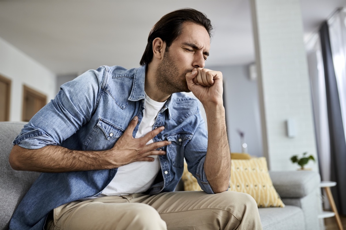 Sick man holding his chest in pain while coughing in the living room.