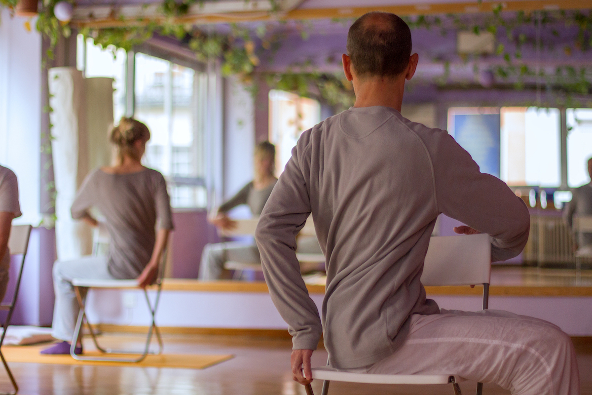 Group yoga class showing people stretching on chairs