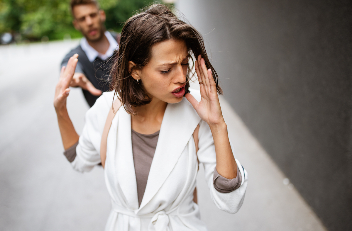 Young couple arguing outside. The woman is in the foreground telling the man to go away.