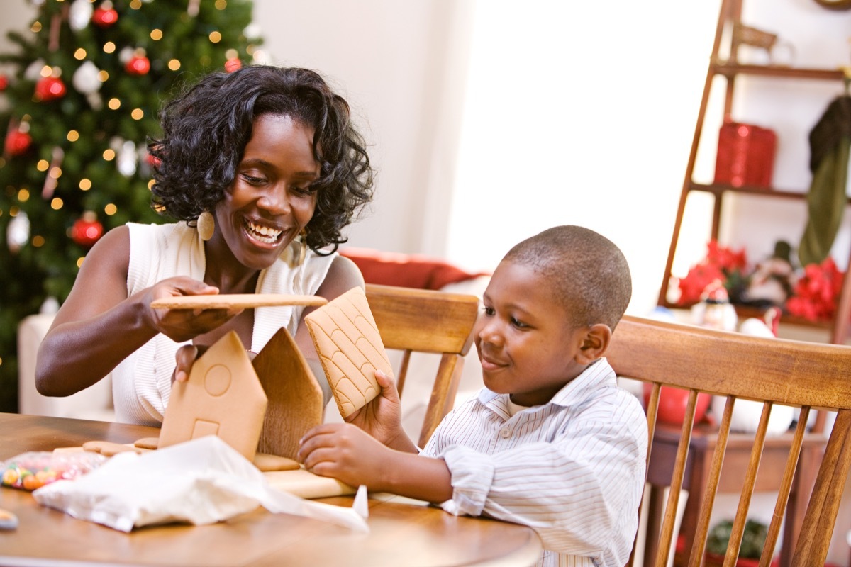 Mother and son building gingerbread house together at kitchen table