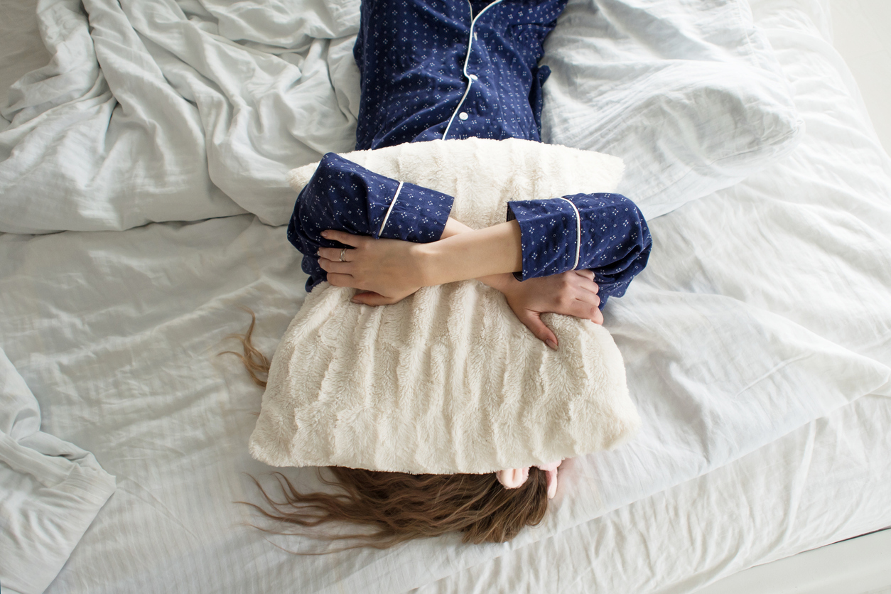 Woman lying in bed with a pillow over her head.