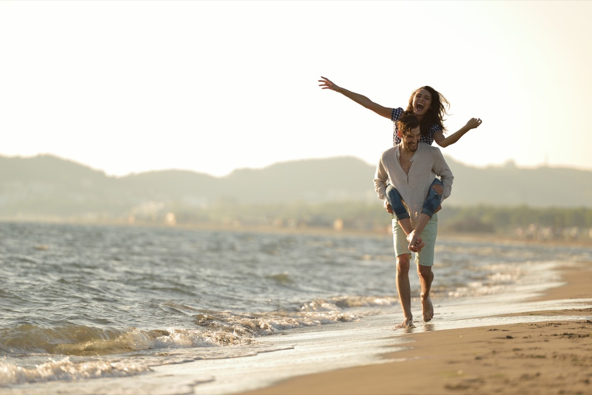 Couple playing around on the beach in the sand.