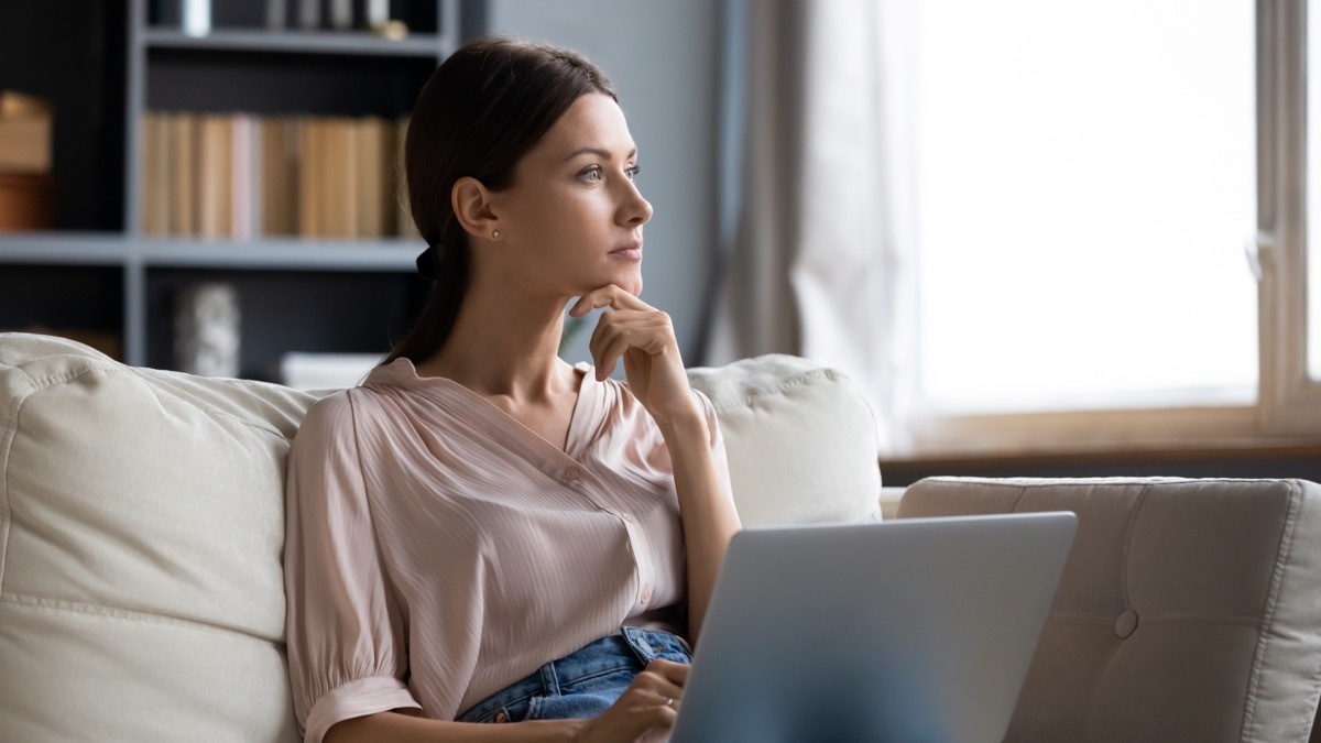 Woman in thought looking up from her laptop.