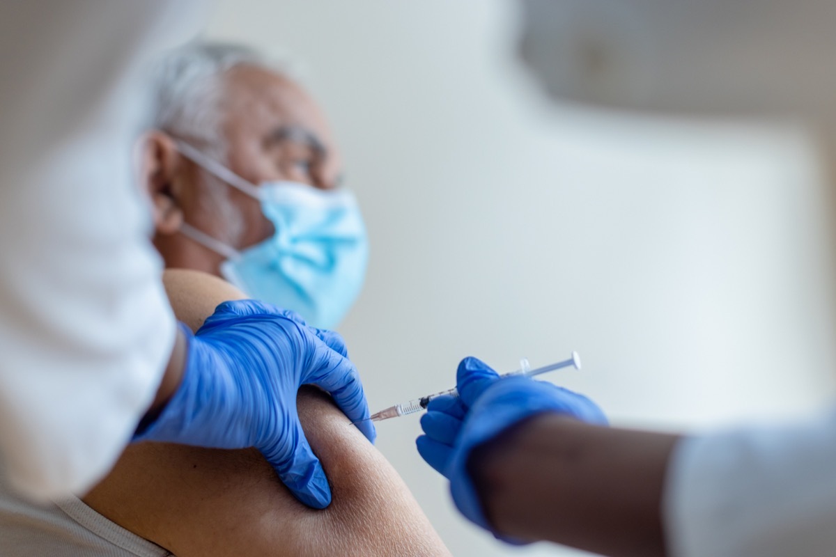 female injecting COVID-19 vaccine to a senior man. Shallow DOF, focus on a foreground