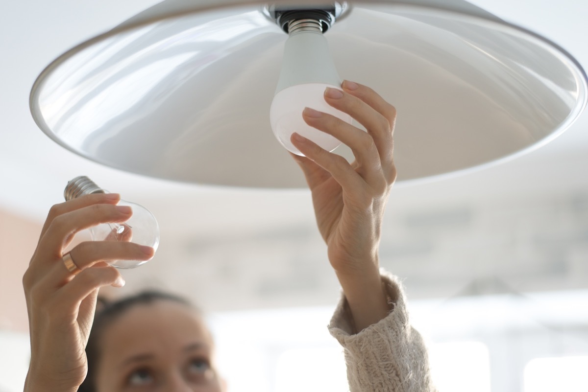 woman installing white lightbulb in home, signs your home is falling apart