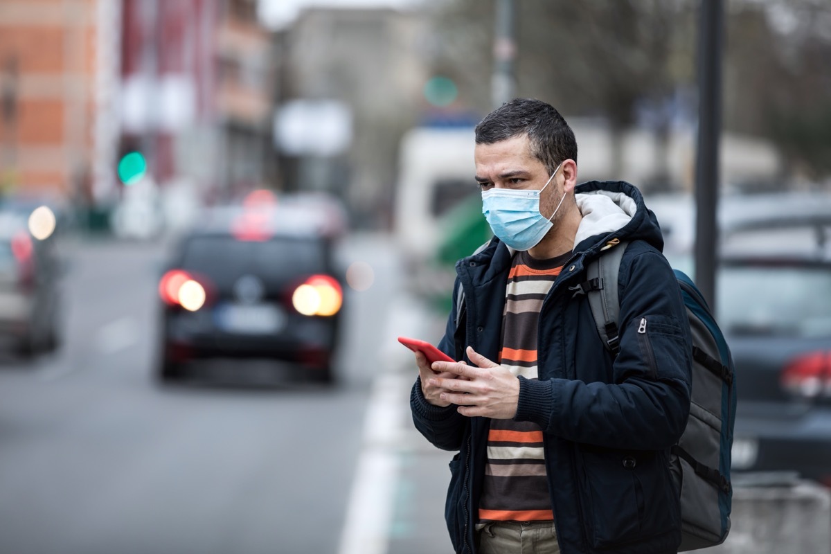 Coronavirus protection. Mature man in the city after the work day, wearing protective mask on the face. Calling for a taxi.