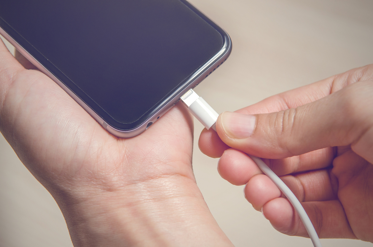 Hands plugging in an iPhone charger into its base