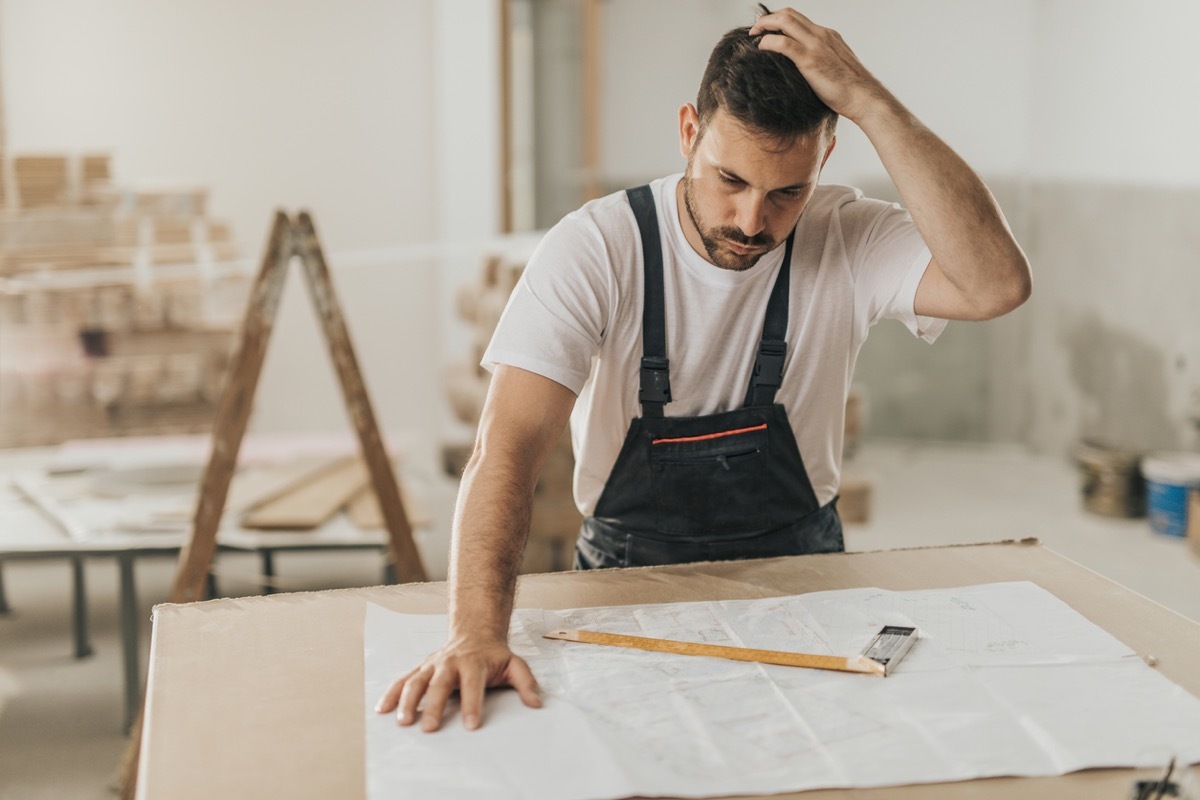 Confused man holding his head while having problems with blueprints during a renovation