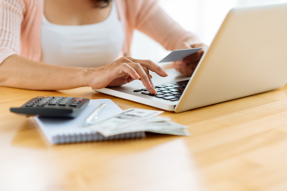 A closeup of someone filing taxes on their laptop with a calculator and a pile of cash