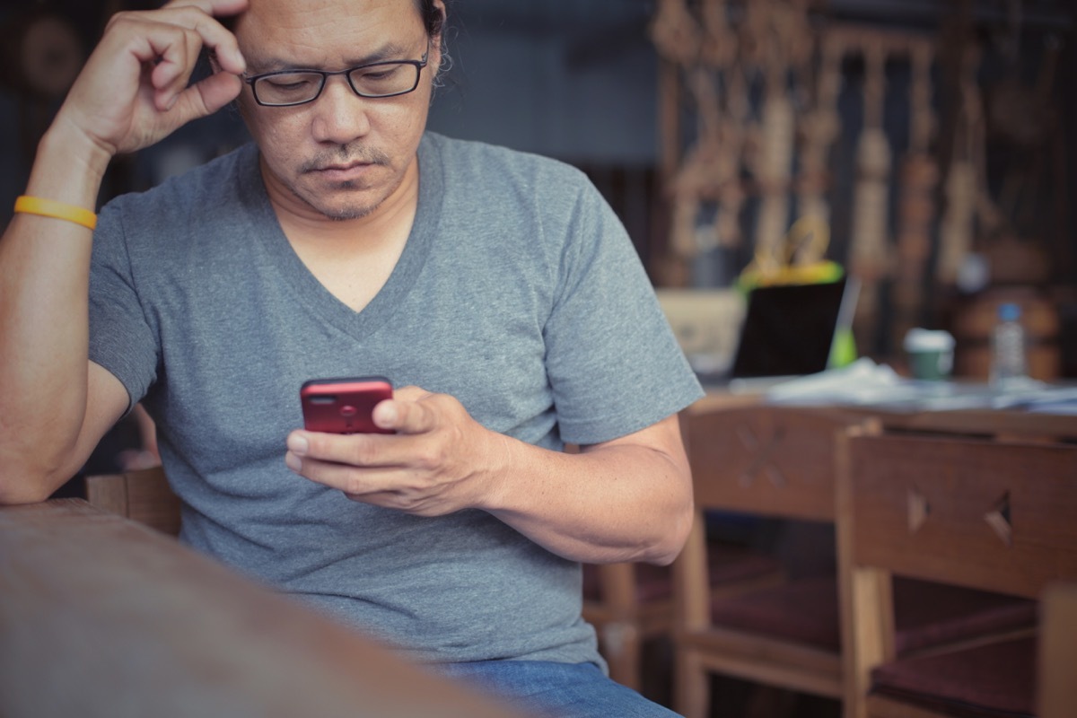 older asian man looking upset at phone