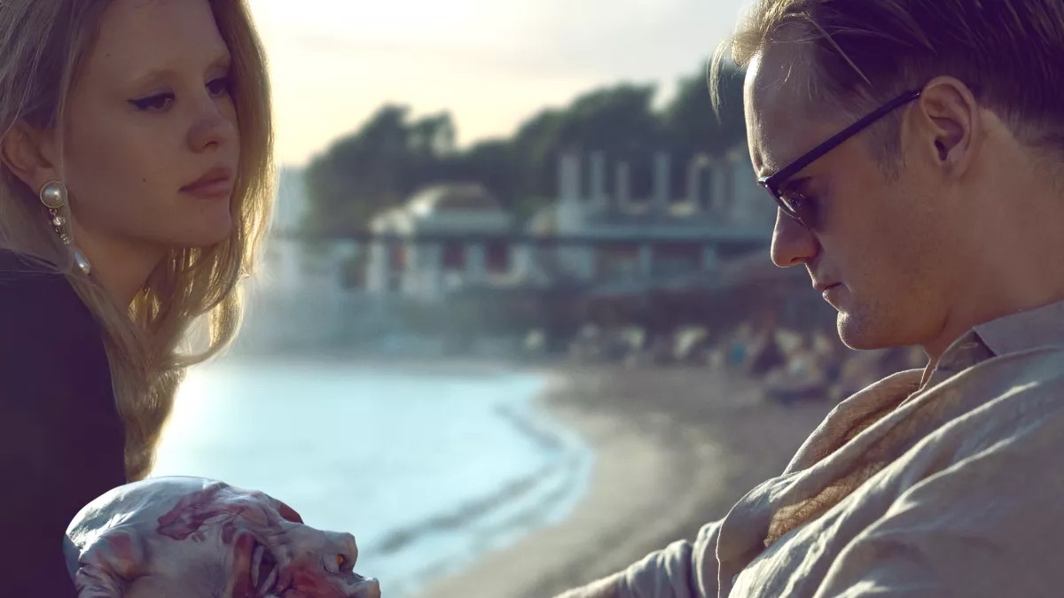 Mia Goth and Alexander Skarsgard sitting by a beach in a scene in Infinity Pool