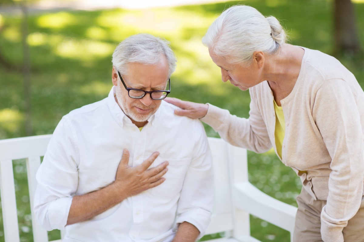 Senior man holding chest and woman checking on him