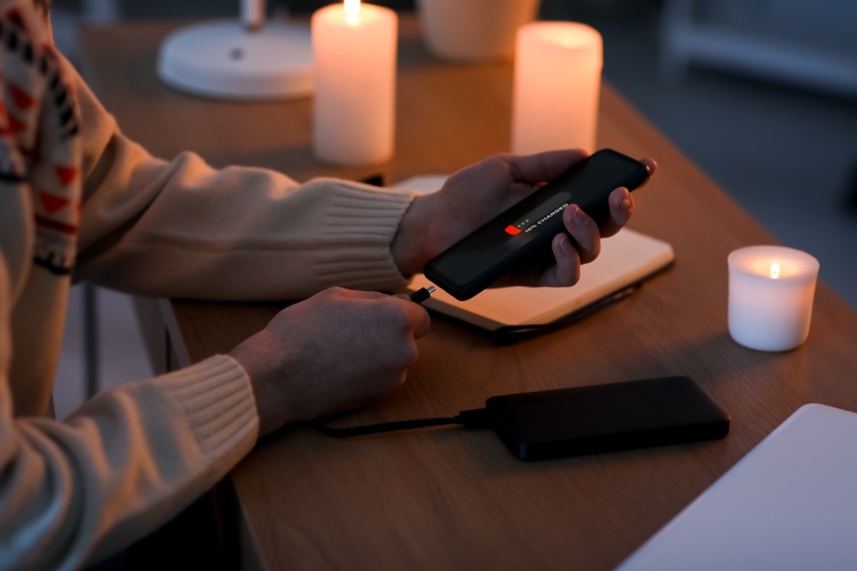 Young man with discharged mobile phone in office during blackout, closeup