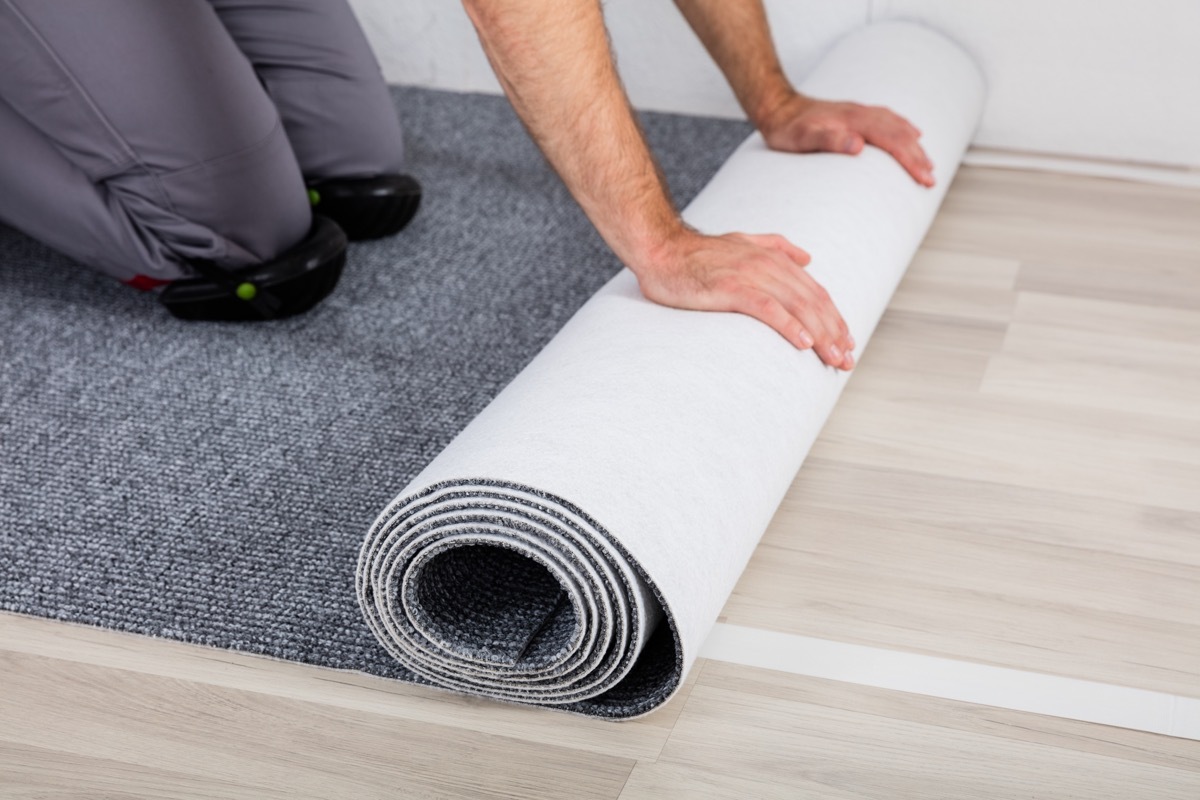 Worker's Hands Unrolling Carpet On Floor At Home