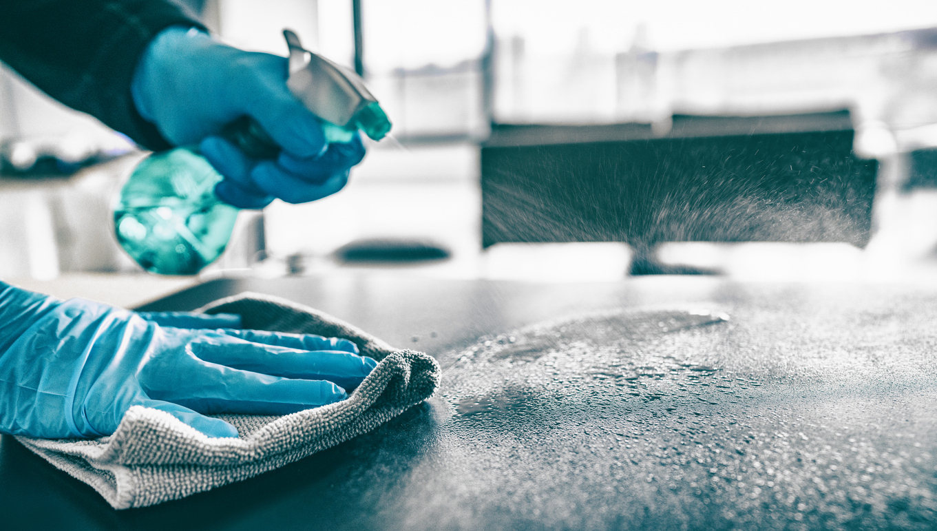 Person sanitizing table with disinfectant cleaner.