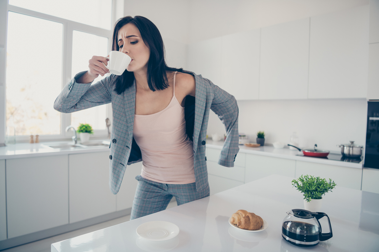 Woman drinking coffee and putting on her sweater in the morning.