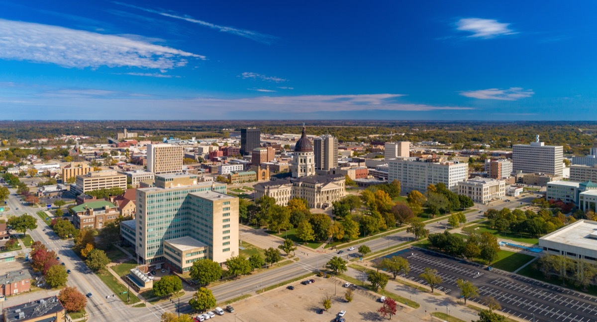 Downtown Topeka aerial skyline view with the Kansas State Capitol building in the center, and a blue sky with clouds in the background.