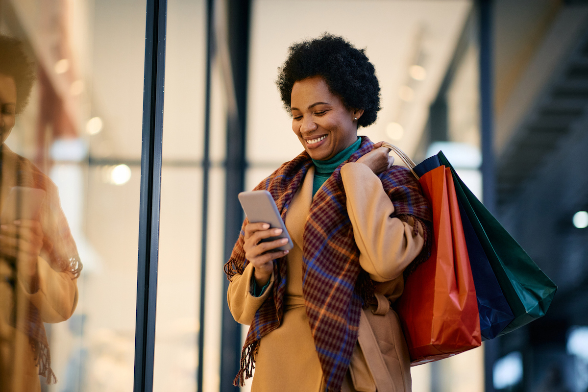 Happy woman with shopping bags using mobile phone while standing in front of a store.