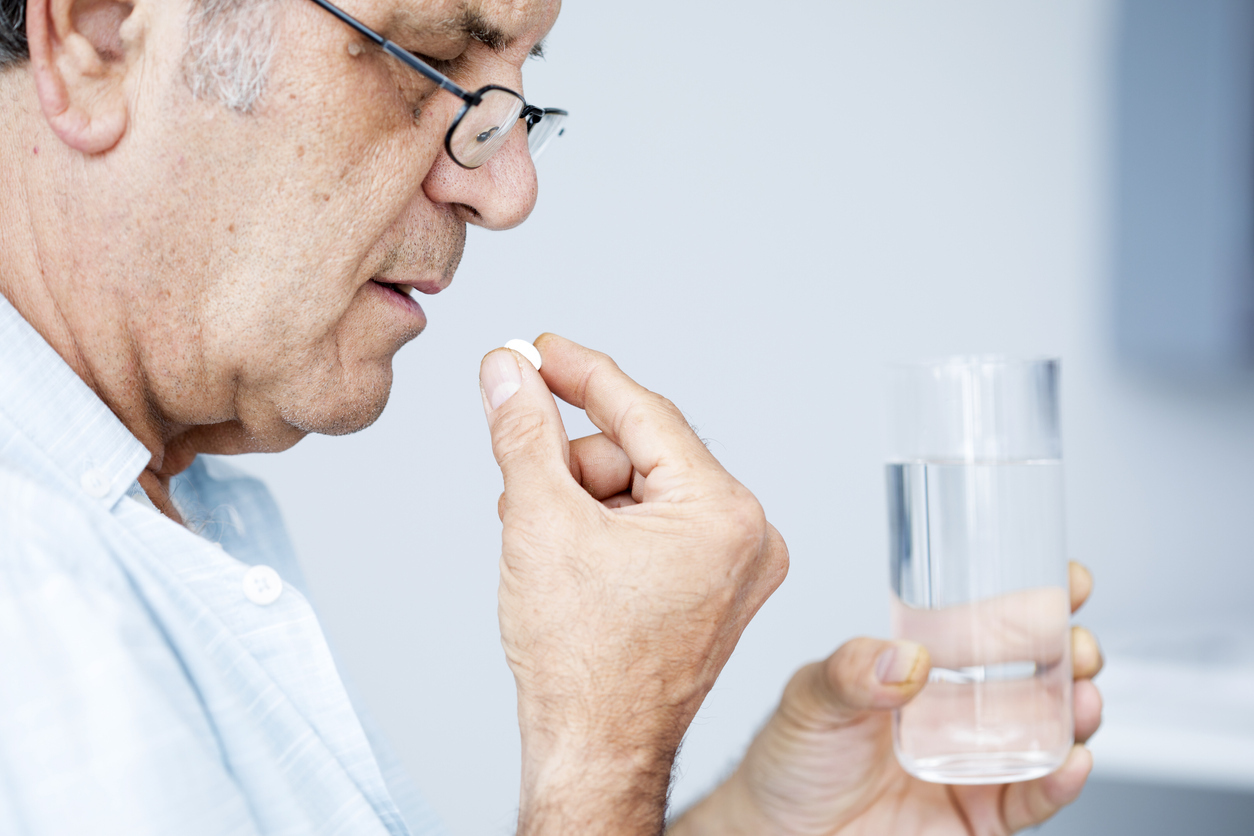 A senior man taking medication with a glass of water