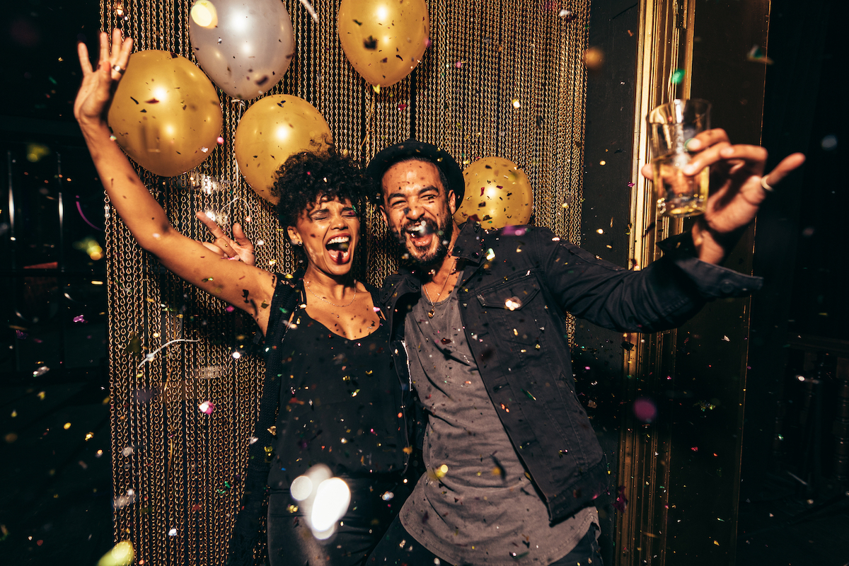 An energetic young couple celebrating the holidays with gold balloons and confetti around them.