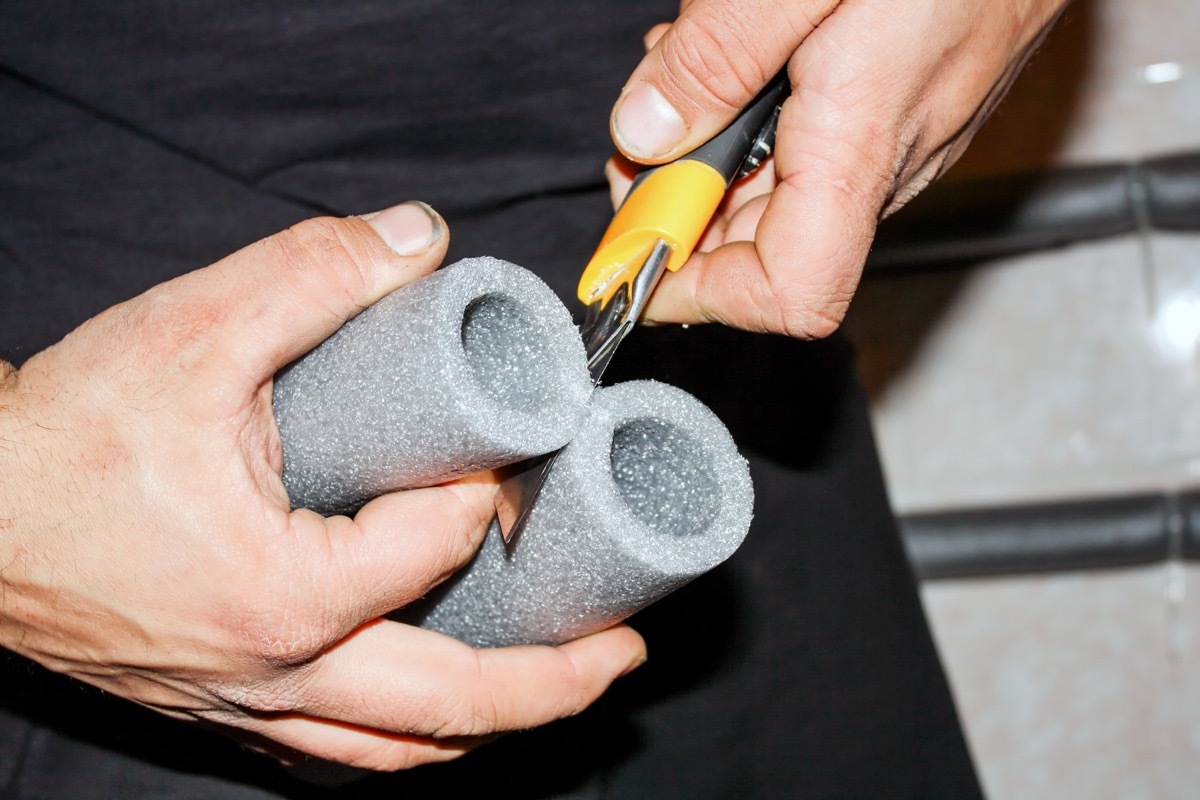 man cutting pipe insulation with black and yellow tool