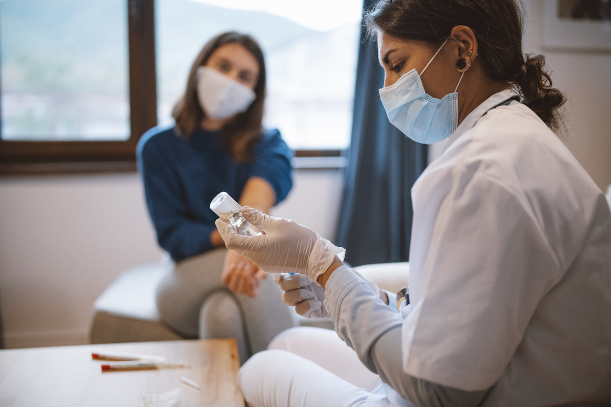 Side view of doctor preparing vaccine syringe to inject on young patient.