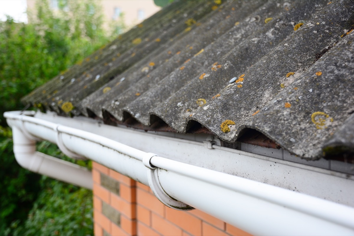 House asbestos roof with close up gutter holder and plastic roof gutter pipe.