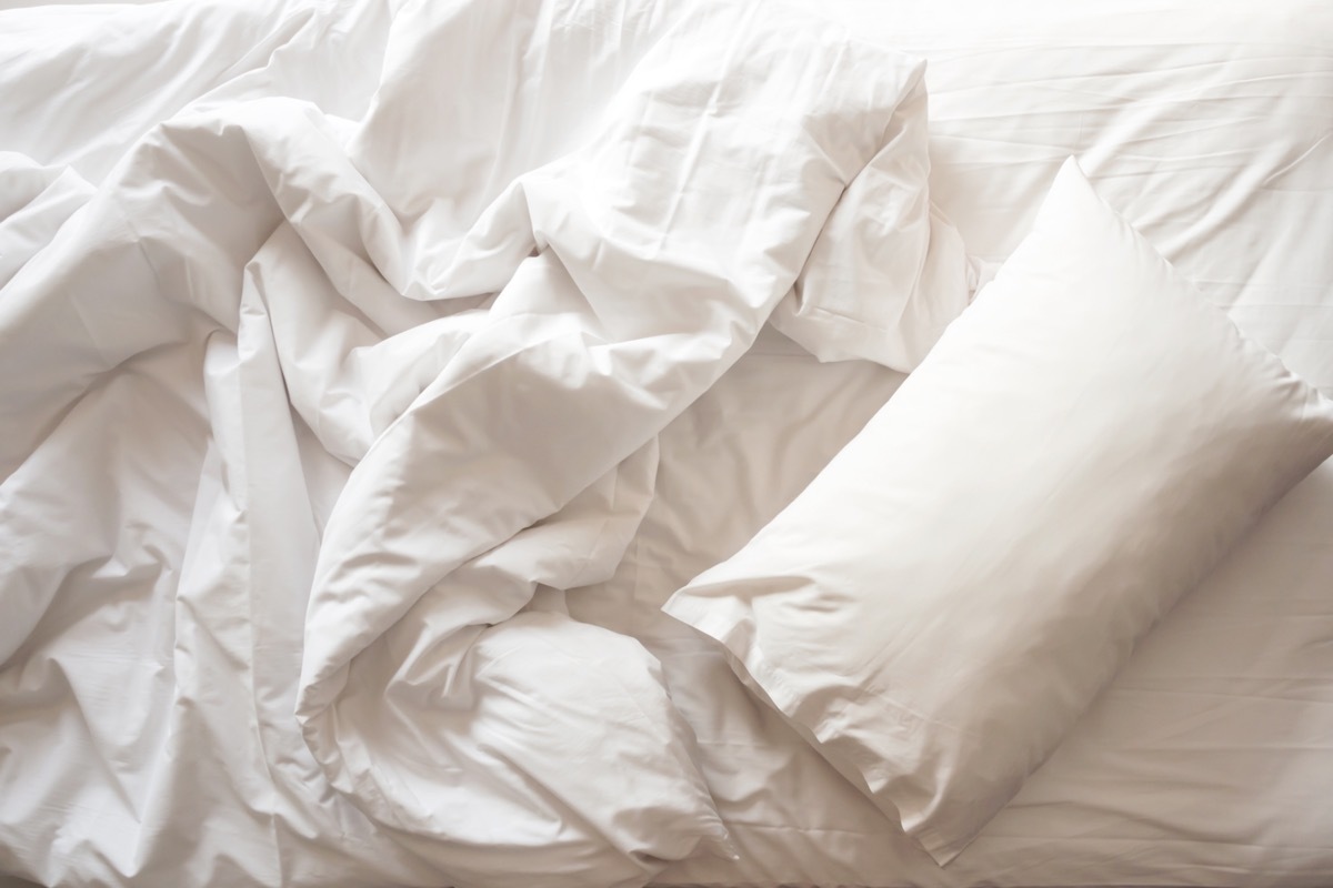 Messy bed. White pillow with blanket on bed unmade. Concept of relaxing after morning. With lighting window. Top view.