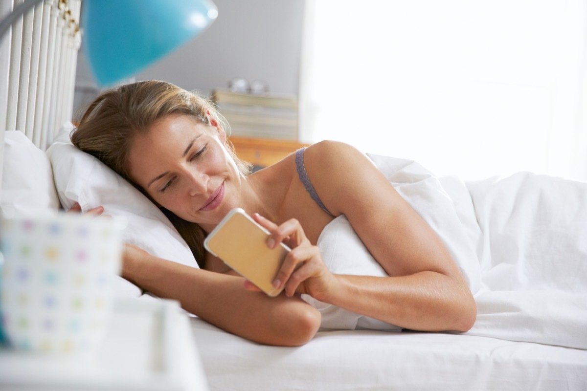 Woman Lying In Bed Reaching To Check Mobile Phone