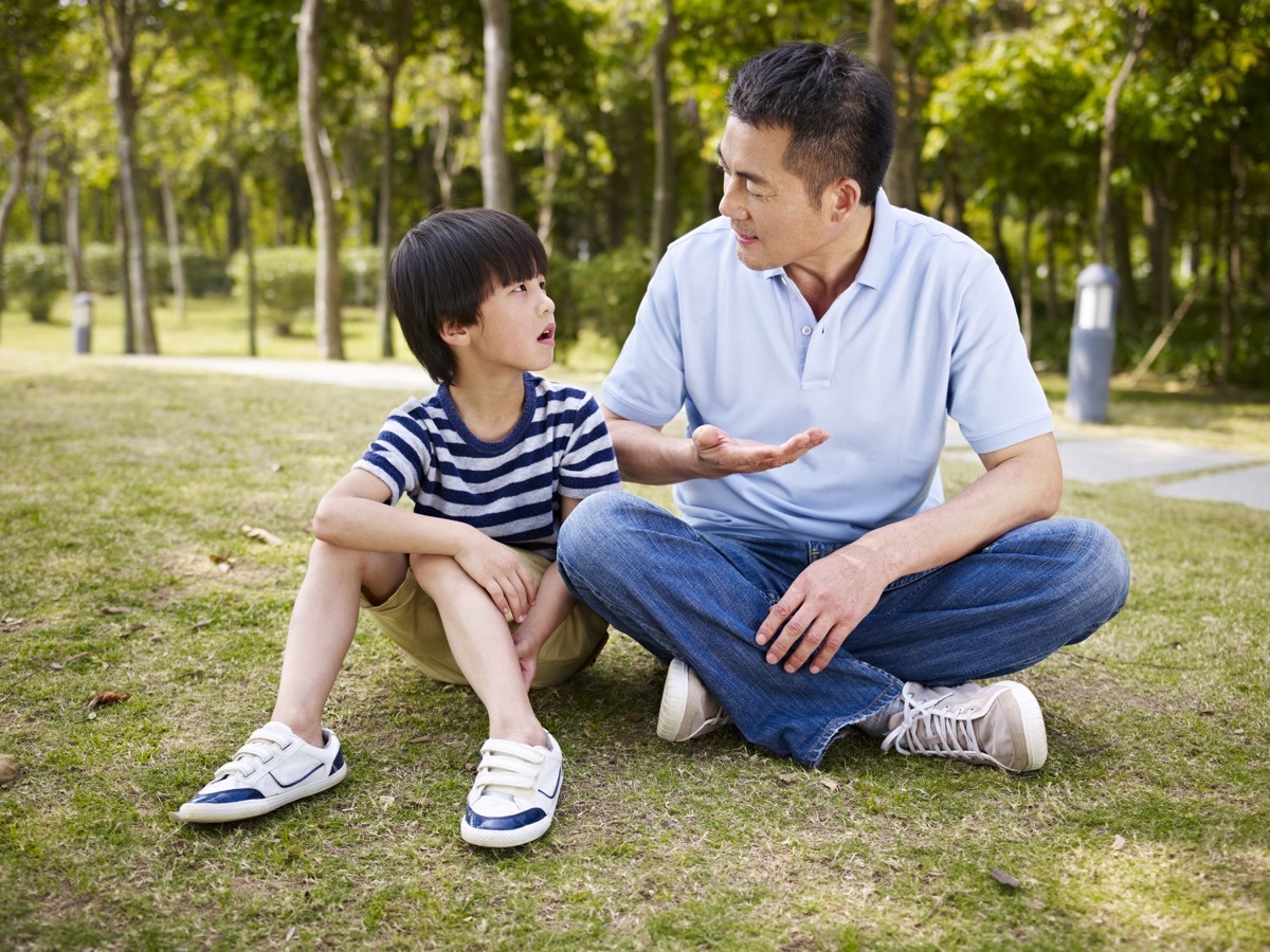 a father and his son sitting on a lawn in a park and talking, prepare children for divorce