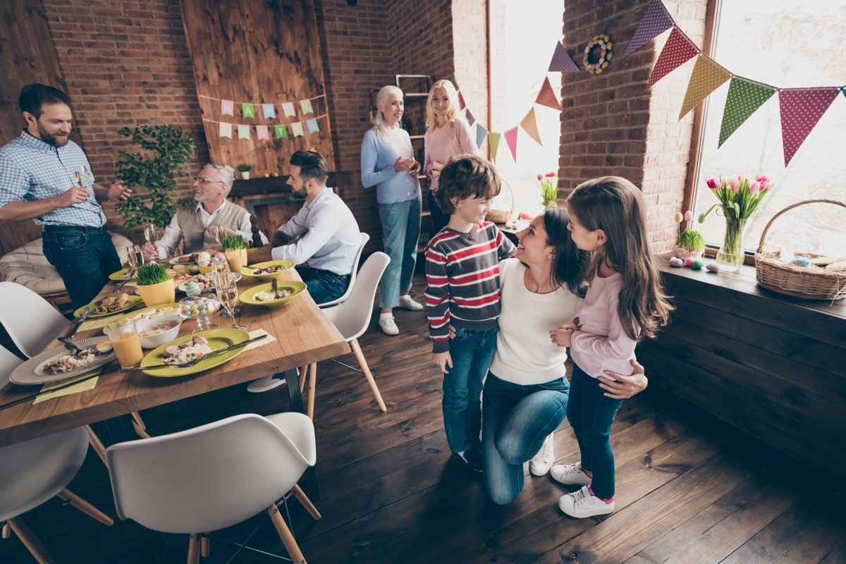 Gathered relatives in decorated house dinner table mom embrace little girl boy children listen to congratulations other communicate talk tell speak