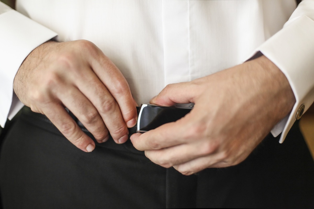 Mid adult unrecognizable man in shirt and trousers fixing his belt buckle