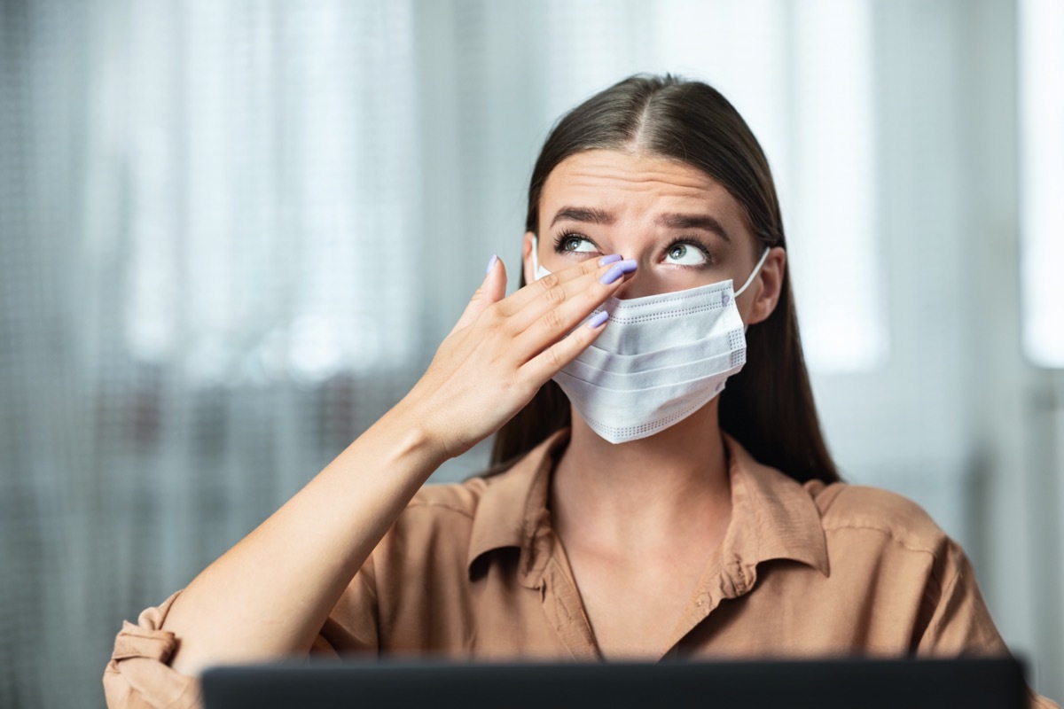 Don't Touch Your Face. Girl wearing surgical mask rubbing her eye with dirty hands, working on laptop