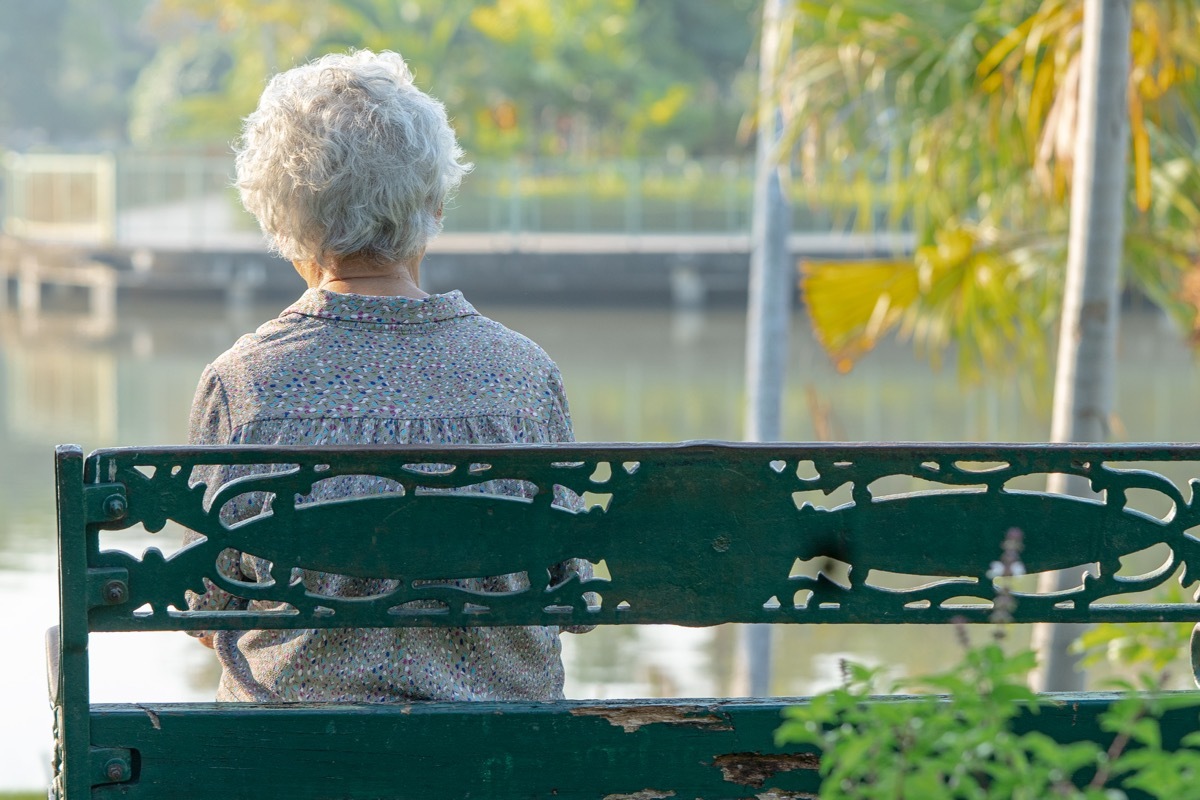 elderly woman depressed and sad sitting back on bench in autumn park.